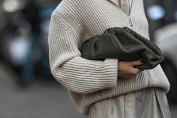 ženska v sivem puloverju drži črno torbico